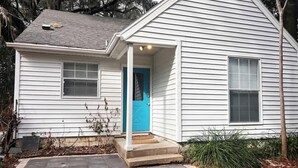A white single-story house with a blue front door, a small porch, and a chimney.