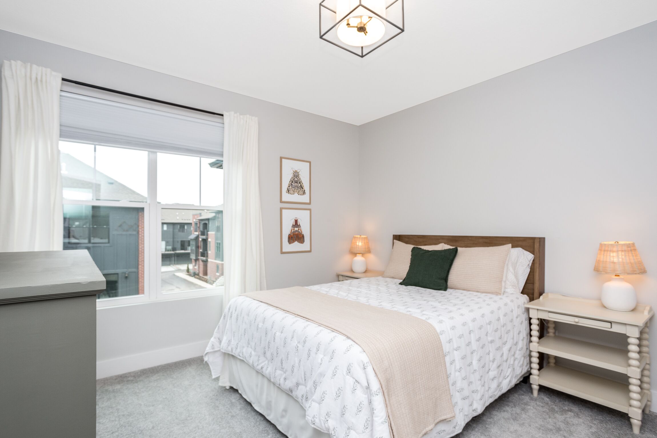 A bedroom with a bed, bedside lamps, a window with curtains, and a view of buildings outside.