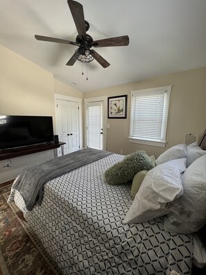 Un dormitorio con cama, ventilador de techo, televisor y ventana con persianas.