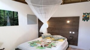 A bedroom with a bed, a canopy, a wooden headboard, a wall-mounted light, and a framed picture. - Le Parc aux Orchidées (Pointe-Noire)