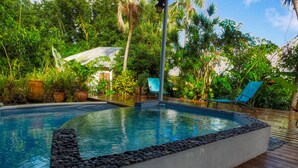 A swimming pool with a wooden deck, surrounded by lush greenery and a covered seating area. - Le Parc aux Orchidées (Pointe-Noire)