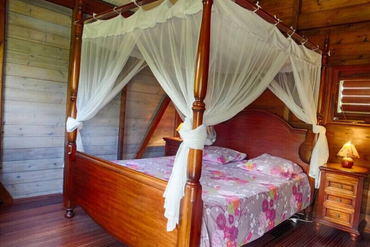 Una cama con dosel de madera, con una colcha estampada con motivos florales y cortinas blancas.