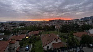 A residential area with houses and a distant view of a sunset over a cityscape. - Le Majestic (Saint-Étienne)