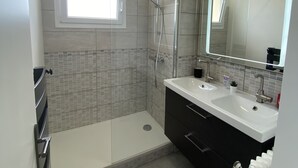 A modern bathroom with a walk-in shower, a large mirror, and a window providing natural light. - Le Majestic (Saint-Étienne)