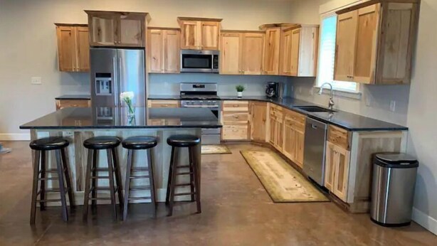 A modern kitchen with wooden cabinets, stainless steel appliances, and a central island with bar stools. - Asixk 1 (Brand New) (Panguitch)