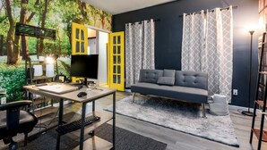 A modern living room with a grey sofa, a wooden desk, and a computer. A yellow door and a TV are visible. - 10 Seat Home theater. Office. Step-Free Entry. Seniors Welcomed. Pet Friendly! (Jim Thorpe)
