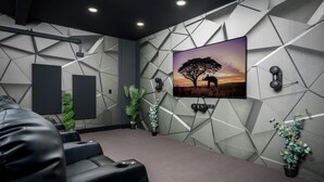 A modern home theater room with a geometric wall design, a mounted TV, and black leather seating. - 10 Seat Home theater. Office. Step-Free Entry. Seniors Welcomed. Pet Friendly! (Jim Thorpe)