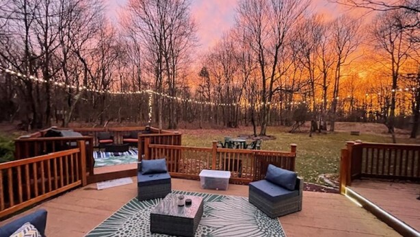 An outdoor deck with seating and a fire pit, surrounded by trees and string lights. - 10 Seat Home theater. Office. Step-Free Entry. Seniors Welcomed. Pet Friendly! (Jim Thorpe)