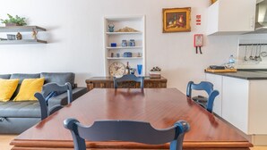 Un coin repas avec une table et des chaises en bois, un canapé avec des coussins, une étagère avec des objets décoratifs et une horloge.