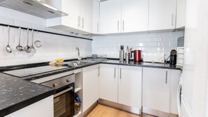 Une cuisine moderne avec des meubles blancs, un plan de travail noir, des appareils en acier inoxydable et des ustensiles suspendus.