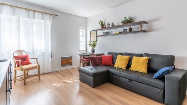 Un salon moderne avec un canapé d’angle, un fauteuil en bois et un coin repas comprenant une table et des chaises.