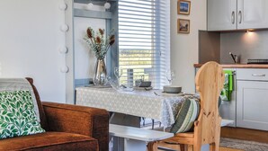 Una cocina moderna con armarios blancos, una mesa de comedor con mantel blanco y un jarrón con plantas secas.