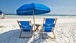 Dos sillas de playa azules con una sombrilla a juego en una playa arenosa.