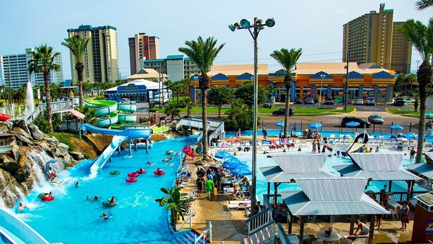 Parque acuático con toboganes y piscinas múltiples, rodeado de palmeras y edificios.