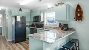 Una cocina con armarios azul claro, un refrigerador negro, encimera de granito y una pequeña estantería de madera con un objeto decorativo.