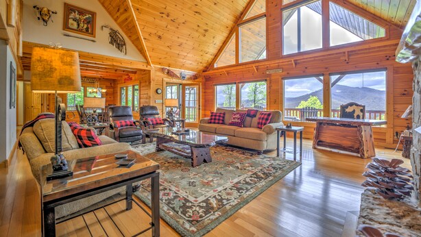 A spacious living room with wooden floors, a high ceiling, and large windows offering views of the outdoors. - Views, Hot Tub, Fire Pit, A Mountain Masterpiece (Maggie Valley)