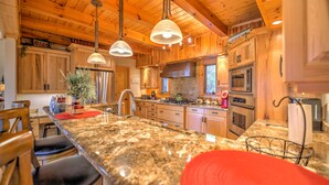 A kitchen with wooden cabinets, granite countertops, stainless steel appliances, and pendant lighting. - Views, Hot Tub, Fire Pit, A Mountain Masterpiece (Maggie Valley)