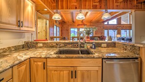 A kitchen with wooden cabinets, granite countertops, stainless steel appliances, pendant lighting, and large windows. - Views, Hot Tub, Fire Pit, A Mountain Masterpiece (Maggie Valley)