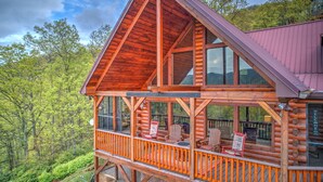 A log cabin with a balcony, large windows, and a view of the surrounding forest. - Views, Hot Tub, Fire Pit, A Mountain Masterpiece (Maggie Valley)