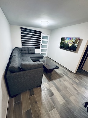 Ein modernes Wohnzimmer mit Ecksofa, Glastisch, Wandfernseher und einer Schiebetür.