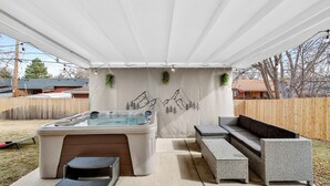 A covered outdoor patio with a hot tub, a sofa, and a dining table.