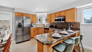 A modern kitchen with granite countertops, stainless steel appliances, wooden cabinets, and a bar area with bar stools.