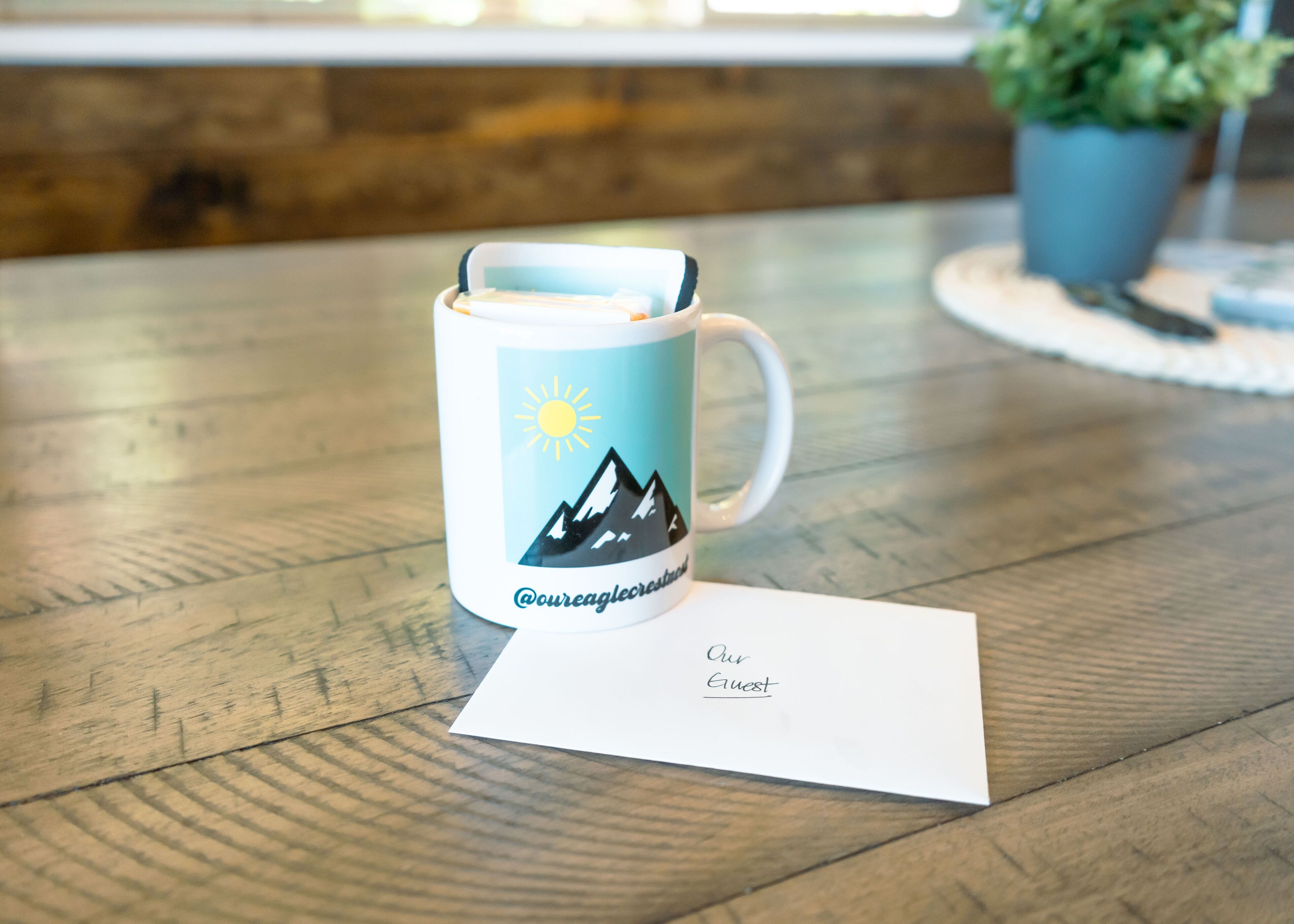 Une tasse blanche ornée d’un motif représentant une montagne et un soleil, posée sur une table en bois.
