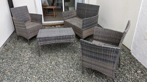 Un coin salon avec des meubles en osier et une porte vitrée donnant sur une pièce.
