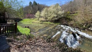 Un río serpentea por un parque con un puente de madera y una zona cubierta de césped.