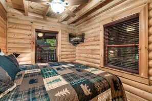 Cozy cabin bedroom with a large bed, wooden blinds, and a flat-screen TV.