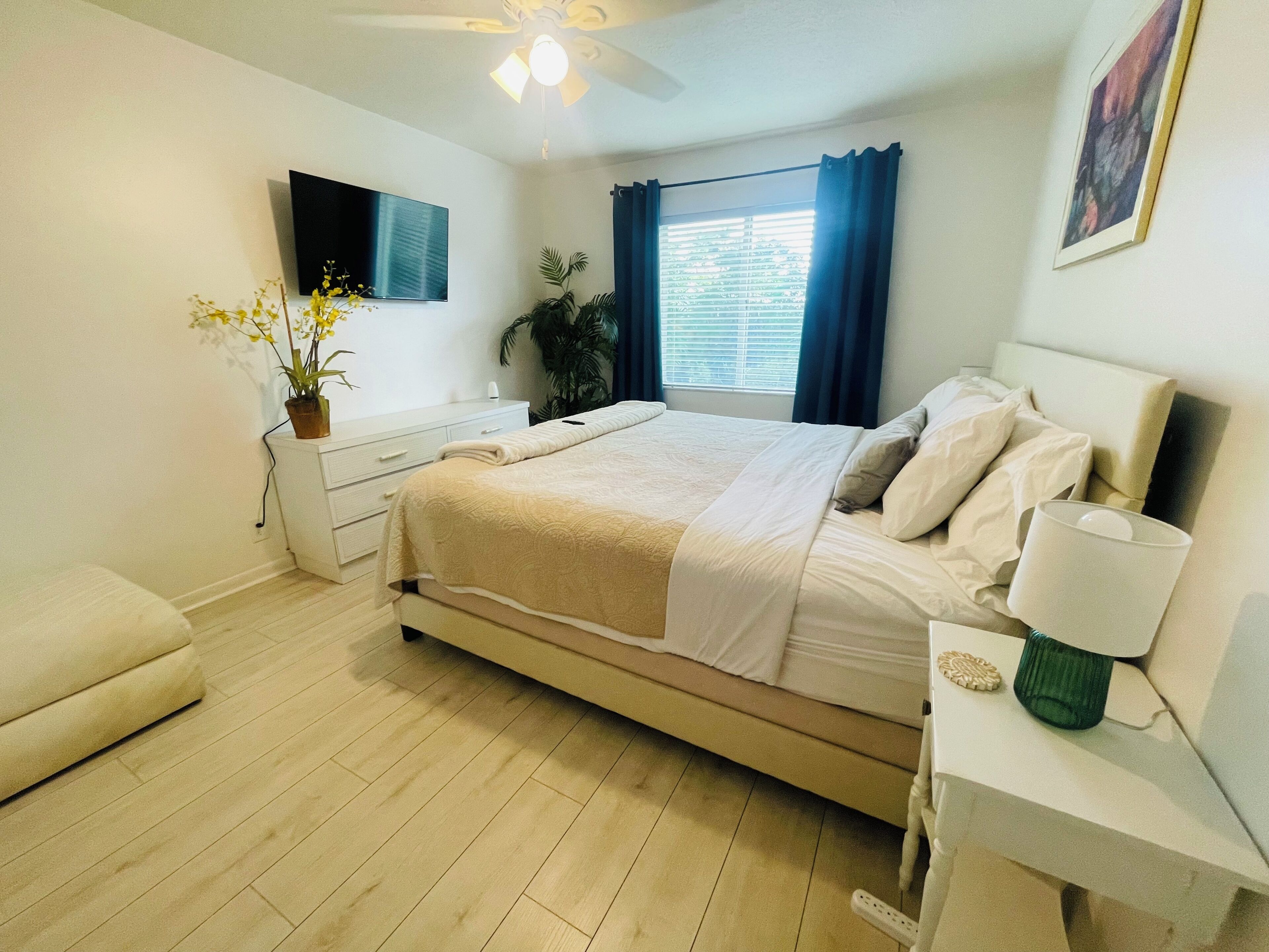 Ein Schlafzimmer mit Bett, Nachttisch, Lampe, Blumentopf und Deckenventilator.