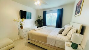 Un dormitorio con cama, mesita de noche, lámpara, planta en maceta y ventilador de techo.