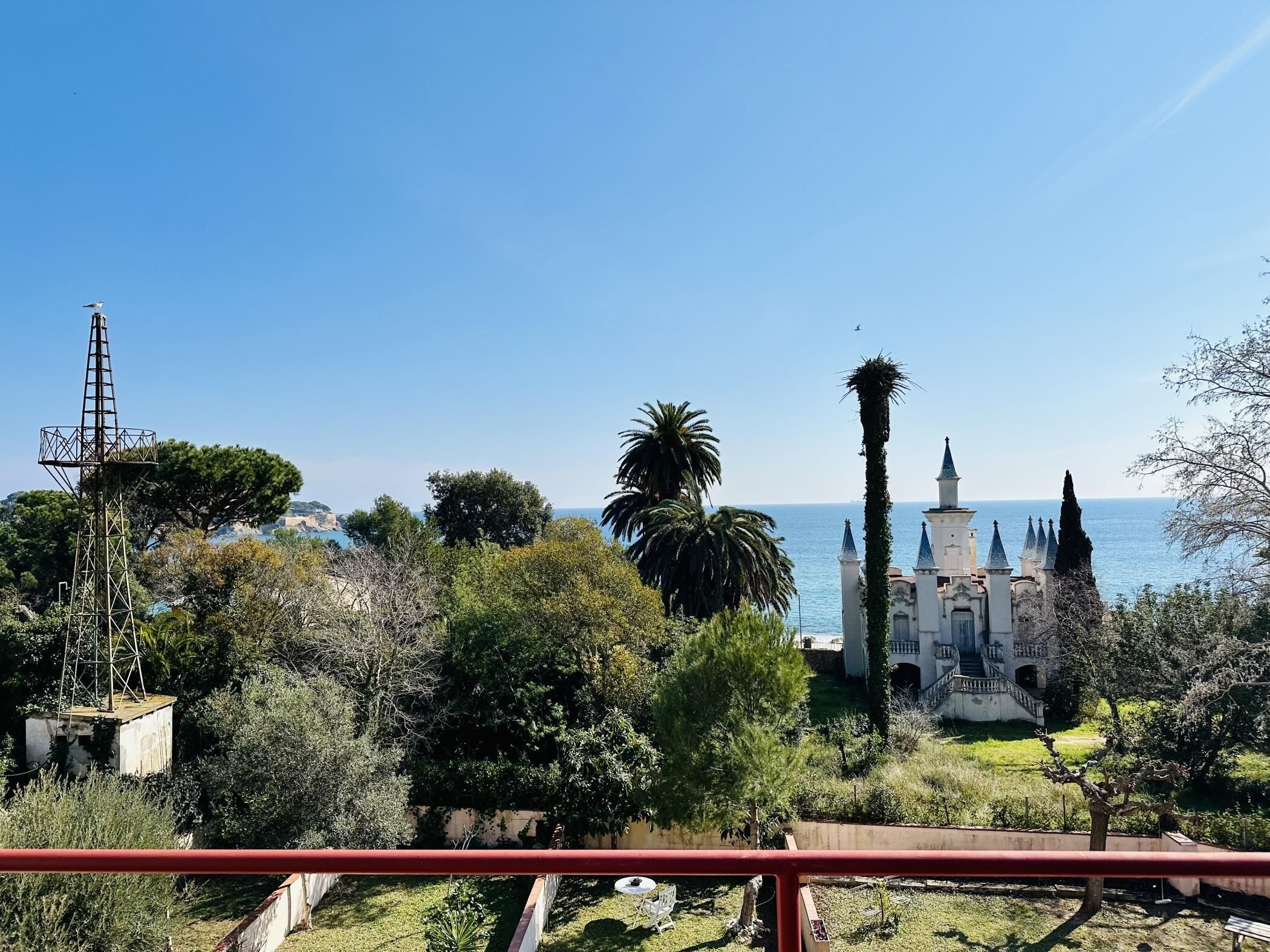 A coastal view with a white building featuring multiple spires, surrounded by lush greenery and a clear blue sky.