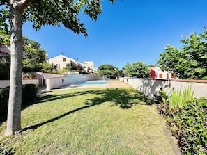 Un barrio residencial con piscina, césped cuidado y un edificio blanco de techo plano.
