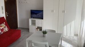 Ein kompakter Wohnbereich mit Esstisch, Stühlen, einem roten Sofa, einem Fernseher und einem Kleiderschrank.