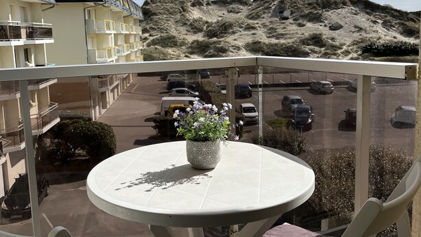 Ein Balkon mit Tisch und Stühlen mit Blick auf einen Parkplatz und eine sandige Landschaft.