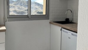 Eine kleine Küche mit Fenster, weißen Schränken, einer Spüle und einem Geschirrspüler.