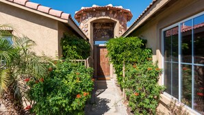 A house with a stone archway entrance, a wooden door, and a pathway leading to the door. - 5 min to Coachella - Boho Chic Oasis with Pool & Spa (Indio)