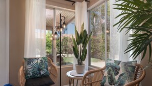 A cozy seating area with wicker chairs and a small table, a potted plant, and a view of greenery outside. - 5 min to Coachella - Boho Chic Oasis with Pool & Spa (Indio)