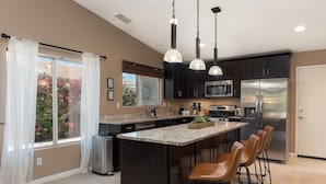 A modern kitchen with a central island, dark cabinets, stainless steel appliances, and pendant lighting. - 5 min to Coachella - Boho Chic Oasis with Pool & Spa (Indio)