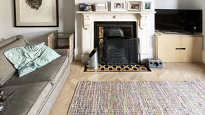 A living room with a fireplace, a sofa, a television, and a patterned rug. - Spacious family townhouse, Telegraph Hill, Summer '23 (London)