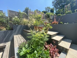 A rooftop garden with various potted plants, wooden steps, and a metal fence. - Spacious family townhouse, Telegraph Hill, Summer '23 (London)