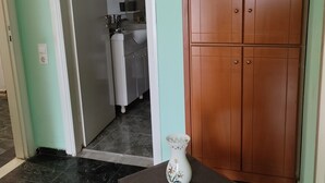 Una habitación con un armario de madera, una mesita con un florero y vistas hacia una zona de cocina.