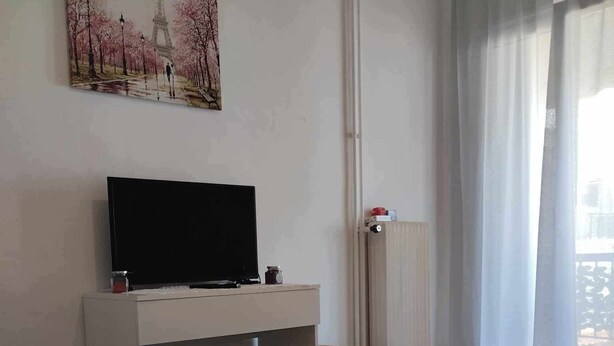 Habitación de hotel con cama, un televisor de pantalla plana sobre un mueble, un cuadro de la Torre Eiffel y una ventana con cortinas.