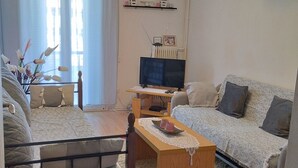 Una sala de estar con un sofá, una mesa de centro, un televisor y una mesita con objetos decorativos.