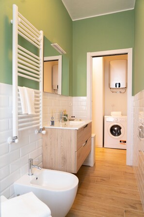 Une salle de bain moderne avec un lavabo blanc, une baignoire sur pieds, un porte-serviettes, un lave-linge et un miroir.