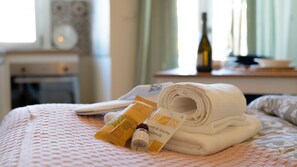 Un lit bien fait, avec des serviettes pliées, un flacon de parfum et une bouteille de vin posés sur une table de chevet.