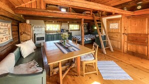Et hyggeligt sommerhusinteriør med et træbord, en sofa, en stige og et tekøkken.