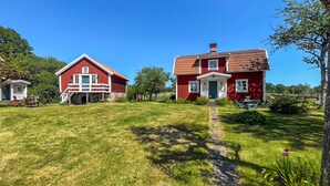 En rød lade med stensokkel og hvid veranda, et rødt hus med grøn dør, og en klar blå himmel.