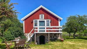 En rød lade med en stenvæg-indgang, en træterrasse og borde med stole udenfor.